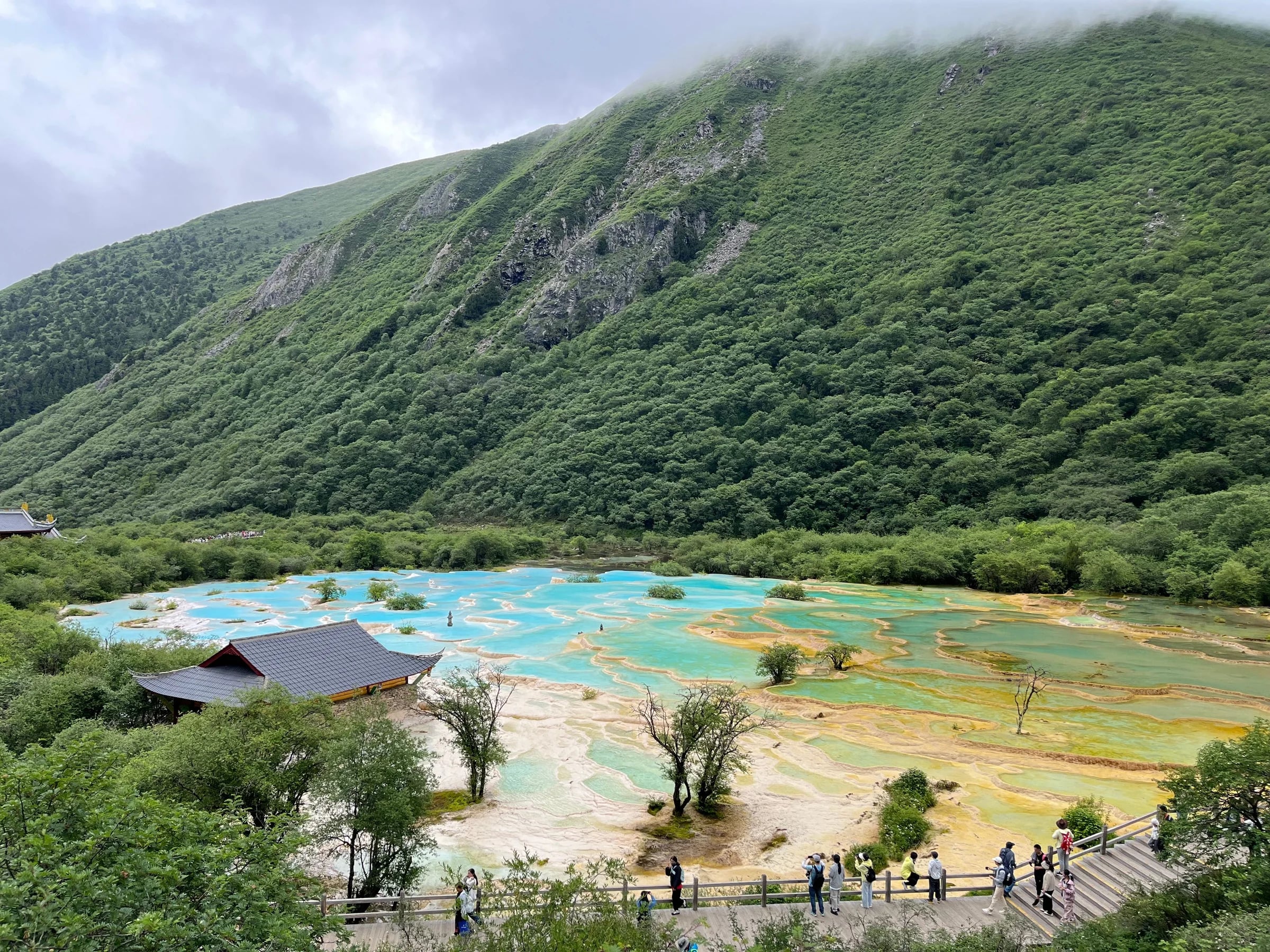 Turquoise terraced travertine pools below a forested mountain in Huanglong