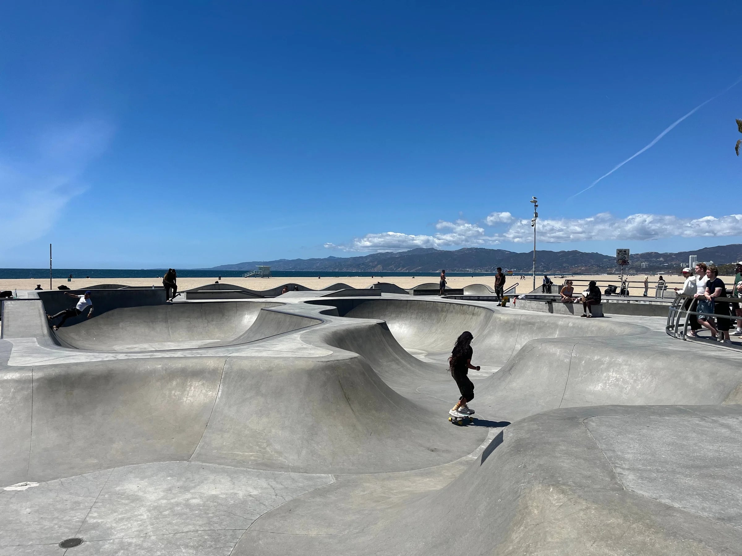 Skaters in the concrete bowls of the Venice Beach skatepark, mountains behind